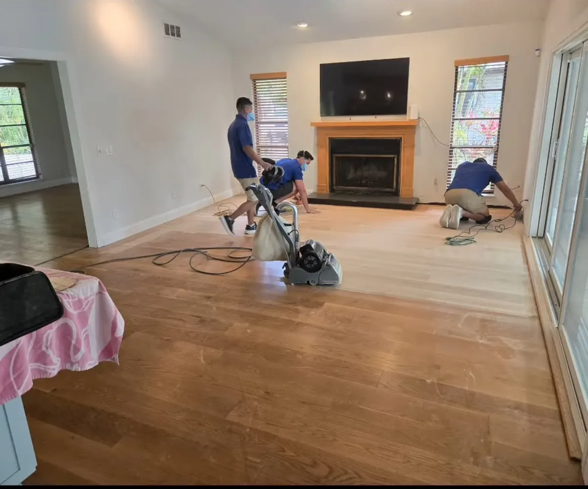 Hardwood floor mid-restoration with sanding equipment in a living room